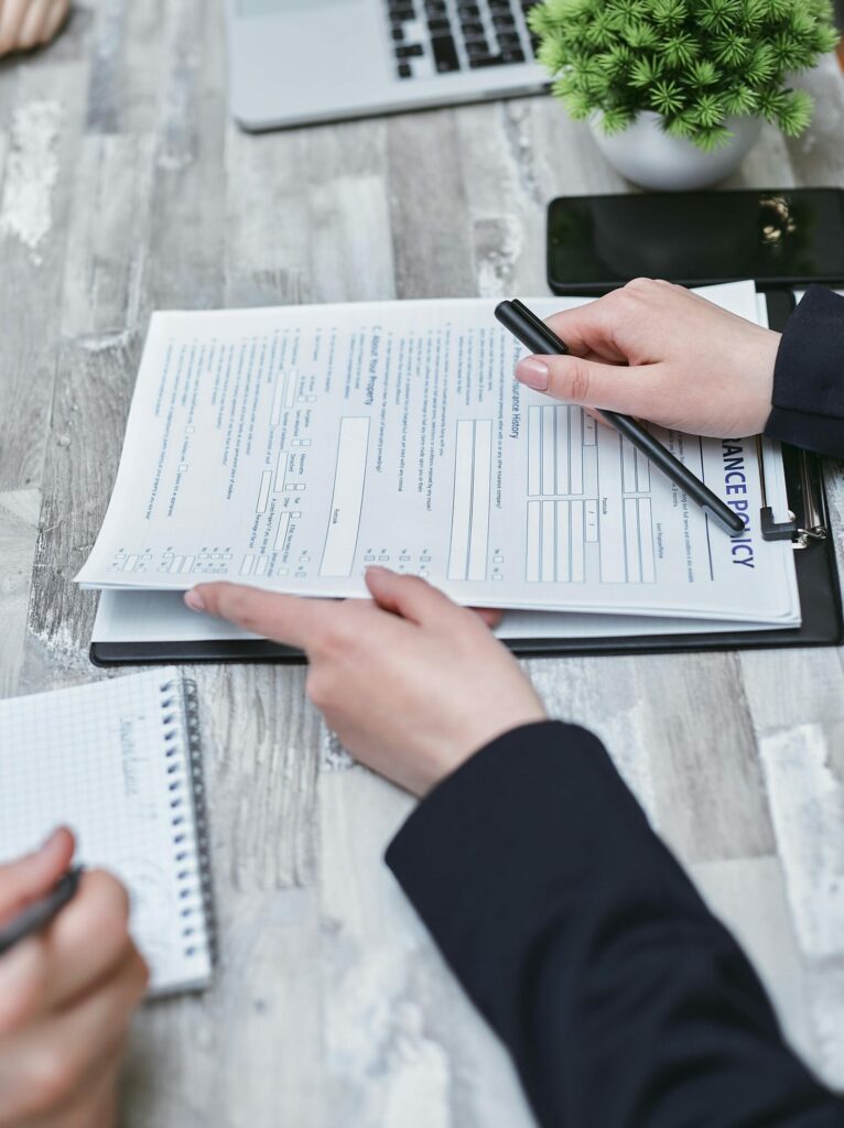 Free Close-up of hands analyzing insurance policy paperwork with pen on table. Stock Photo